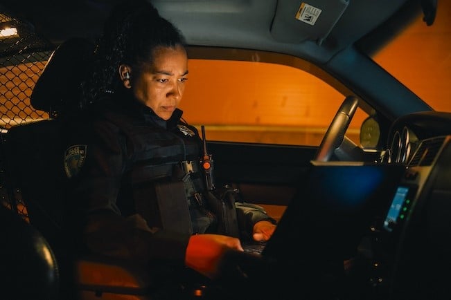 female officer sitting in police cruiser looking at laptop